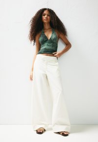 Green tie-dye halter top paired with wide-leg white pants and black platform sandals. Model has voluminous curly hair.
