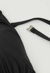 Czarny strój kąpielowy wykonany z gładkiego, elastycznego materiału. Regulowany pasek z metalowym zapięciem. Zbliżenie podkreślające teksturę i wzór.