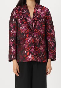 Blazer floreale in tessuto scuro con motivi di foglie metallizzate rosse e viola, revers a punta e due tasche frontali. Fit strutturato e sartoriale.