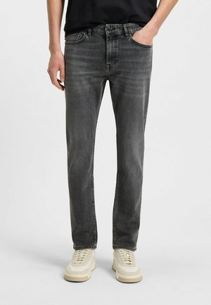Verbleekte zwarte denim jeans met een recht silhouet, vijf zakken en contrasterende stiksels. Gecombineerd met lichtgekleurde sneakers.