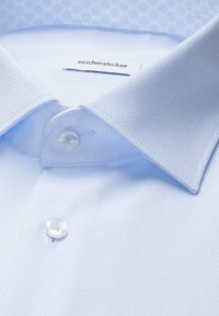 Chemise habillée bleu clair texturée avec col pointu et boutons blancs, étiquetée "seidensticker" à l'intérieur du col.