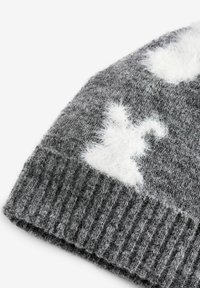 Bonnet tricoté gris avec une texture côtelée et des accents blancs duveteux. Présente un matériau doux et une vue en angle montrant le rebord replié.