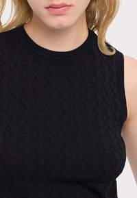 Top senza maniche nero in maglia con un motivo a diamante testurizzato, scollo rotondo e bordi a coste. Tessuto morbido con una leggera elasticità.