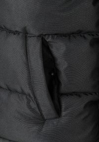Sección de chaqueta acolchada negra con un bolsillo en la costura lateral. Tejido texturizado, resistente al agua, con costuras visibles y ligero brillo.