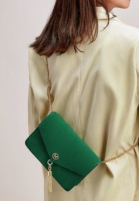 Borsa a tracolla verde in suede con tracolla in oro, dotata di chiusura a pattina e un accento a frange. Texture liscia e forma rettangolare.