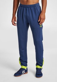 Marinblå sportbyxor med en strukturerad tyg, med ljusgröna sidosträcker och en broderad logotyp på övre låret.