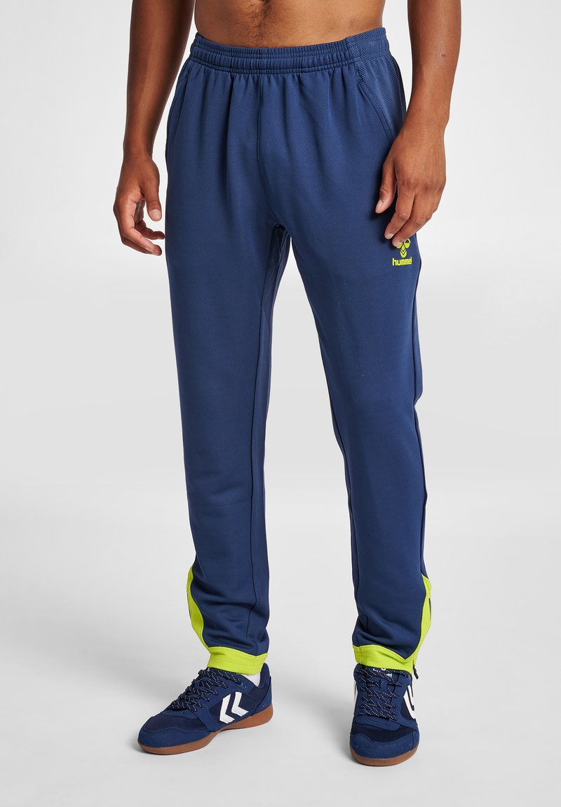 Marinblå sportbyxor med en strukturerad tyg, med ljusgröna sidosträcker och en broderad logotyp på övre låret.