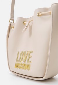 Beige syntetisk bucketväska med detaljer i guldton, dragsnörning och präglad "LOVE MOSCHINO"-logotyp på framsidan.