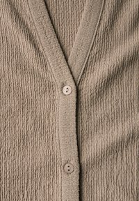 Beige texturovaný cardigan s výstřihem do V, který má žebrovaný povrch a jedno světle zbarvené zapínání na knoflík na přední části.
