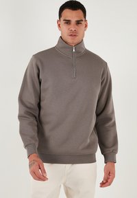 Hallide, pehmeast kangast valmistatud hall zip-up dressipluus, millel on pikad varrukad, soonikud mansettides ja sile tekstuur. Lihtne disain minimaalsete aktsentidega.