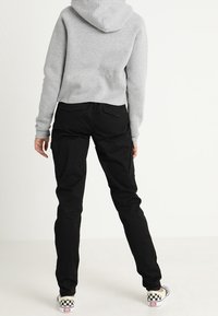 Grijze cropped hoodie met een capuchon, gecombineerd met zwarte slim-fit broeken. De broeken hebben zijzakken en worden gedragen met schoenen met een schaakbordpatroon.