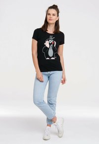 Black t-shirt featuring a cartoon mole graphic in gray and orange, worn with light blue jeans and white sneakers. Simple design, short sleeves.