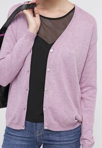 Light purple cardigan made of soft material, featuring a loose fit, round neckline, and silver buttons. Worn over a black mesh top.