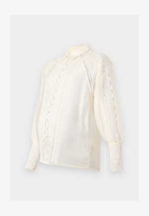 Balta bluzė su nėrinių detalėmis ant rankovių ir priekinės dalies. Yra apykaklė, dekoratyviniai mygtukai ir tekstūruotas audinys, taip pat pūstomis rankovėmis.