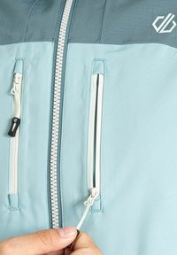 Hellblaues Jacket mit einem grauen oberen Abschnitt, Frontreißverschluss und zwei seitlichen Reißverschlusstaschen. Weicher Stoff mit glatter Textur.