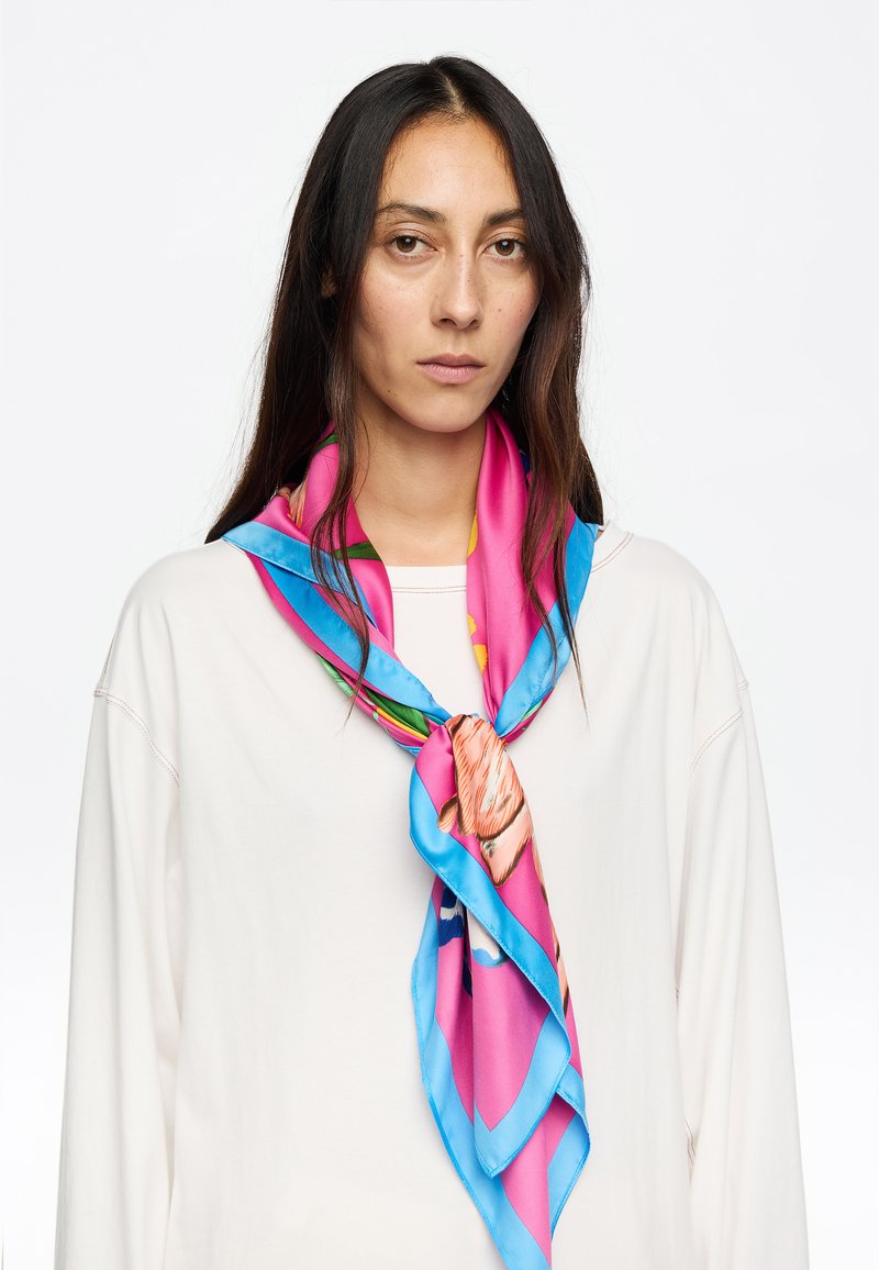 Foulard di seta con colori vivaci di rosa e blu, decorato con motivi floreali. Texture liscia, annodato attorno al collo in uno stile stratificato.