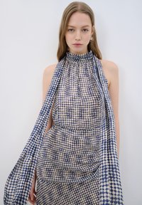 Robe dos nu en tissu transparent avec un motif de pois bleu et crème, dotée de détails froncés et d'un foulard attaché fluide.