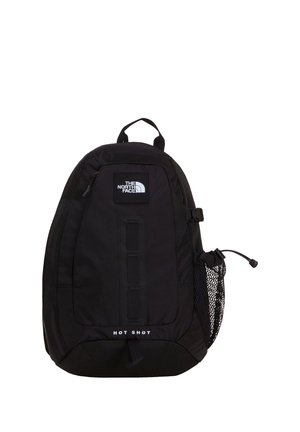 Sac à dos noir North Face Hot Shot avec poche avant zippée, porte-bouteille latéral en mesh et poignée de transport supérieure sur fond blanc.