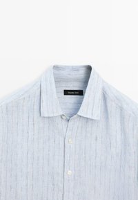 Camicia a righe azzurra con colletto button-up, con un'etichetta che reca la scritta "Massimo Dutti." Lo sfondo è bianco semplice.