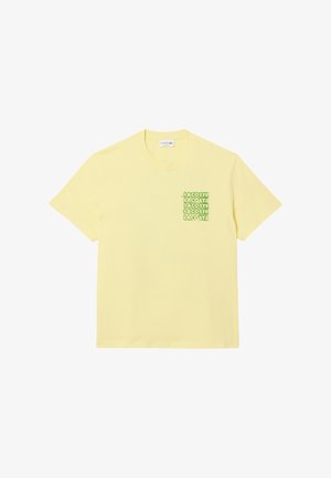 Camiseta de algodón amarilla con un pequeño estampado gráfico verde de la palabra "LACOSTE" en la parte izquierda del pecho. Diseño de mangas cortas y cuello redondo.