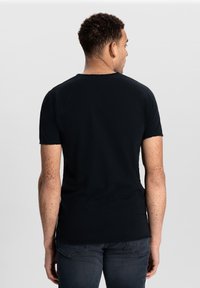 Černé bavlněné tričko s krátkými rukávy, kulatým výstřihem a slim fit. Viditelné švy a detail textury na látce.