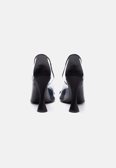O pereche de pantofi negri cu toc înalt și părți laterale transparente, văzuți din spate pe un fundal alb simplu.