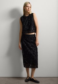 Zwart kanten two-piece set met een mouwloze top en een rok tot de knie, beide met ingewikkelde bloempatronen en een taillering.