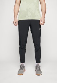 Černé sportovní kalhoty s zúženým designem, vyrobené z lehkého materiálu. Na levé straně se nachází bílé logo Nike.