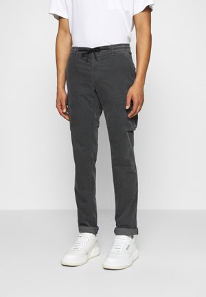 Grijze cargobroek met een tailleband met koord, getailleerd ontwerp, zijzakken en afgeronde broekspijpen, gecombineerd met witte sneakers en een wit T-shirt.