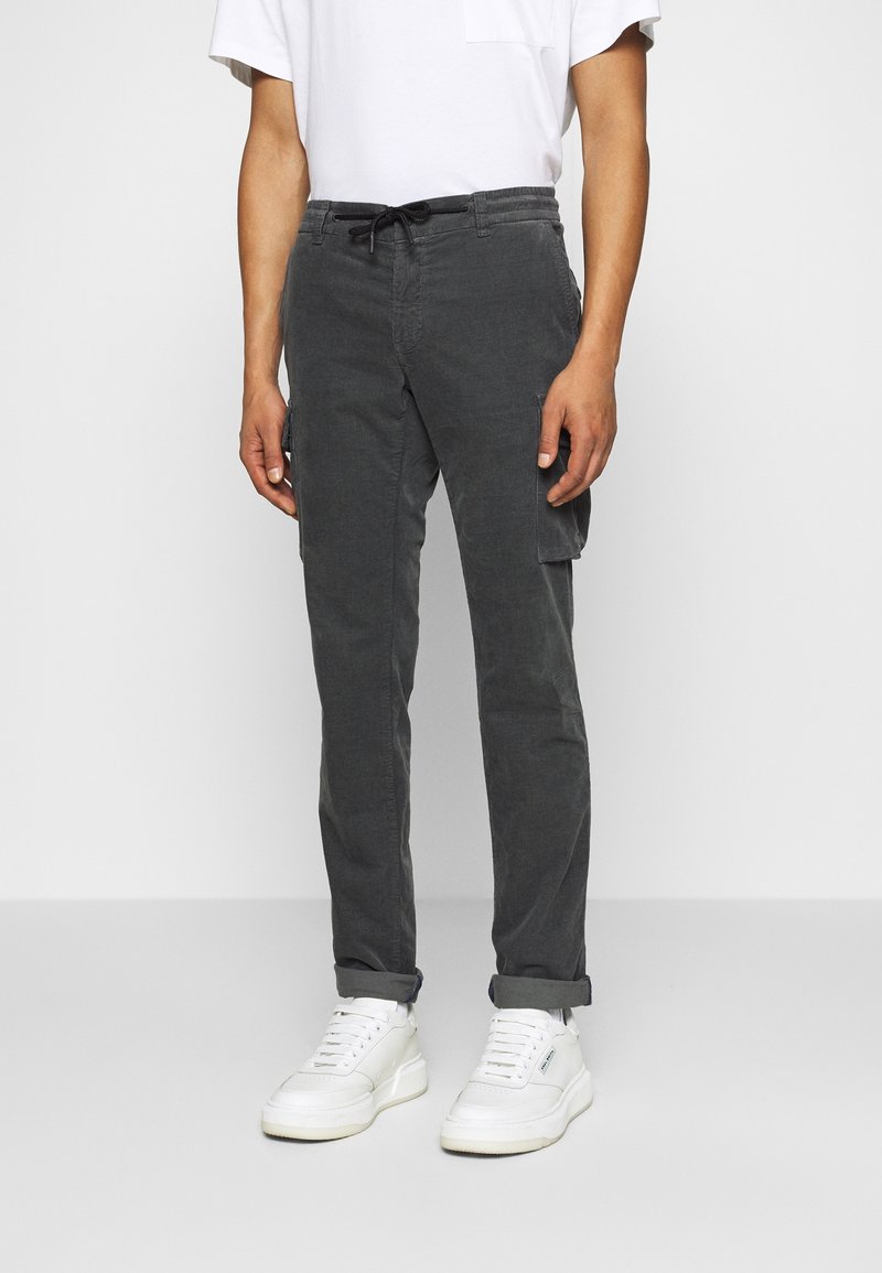 Szare spodnie cargo z elastycznym paskiem w talii, zwężanym krojem, bocznymi kieszeniami i wykończeniem przy nogawkach, w zestawieniu z białymi trampkami i białą koszulką.