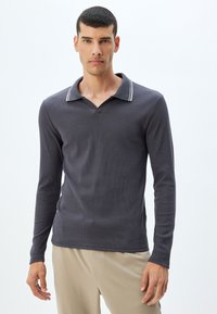 Katoenen polo met lange mouwen in donkergrijs met een geribbelde textuur, voorzien van een V-hals en contrasterende gestreepte kraagdetails.