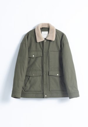 Chaqueta verde oliva con un cuello de piel beige, que cuenta con cuatro bolsillos frontales, botones a presión y un acabado de tela texturizada.