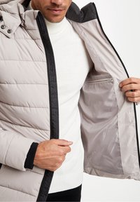 Světlá šedá prošívaná bunda s černým zipem a límcem. Vnitřek má hladkou látkovou podšívku a zipovou kapsu na pravé straně.