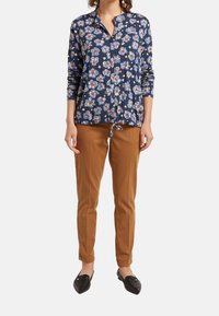 Blusa floral azul marino con mangas largas y cintura ajustable, combinada con pantalones ajustados color cáñamo. El calzado es negro con textura acolchada.