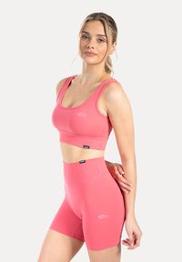 Roze sportbeha en short met hoge taille, gemaakt van rekbare stof. Heeft een eenvoudig ontwerp met een logo aan de voorkant. Glad oppervlak.