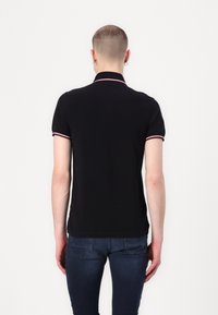 Polo negro con cuello acanalado que presenta bordes rojos y blancos. Mangas cortas con acentos similares. Ajuste estándar y material de mezcla de algodón.