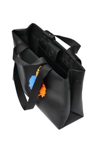 Zwarte draagtas gemaakt van duurzaam materiaal, met een gestructureerd oppervlak, stoffen hengsels, een drukknoopsluiting en een kleurrijk pompon sleutelhanger eraan bevestigd.