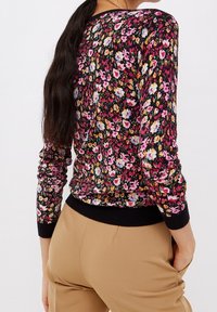 Pull à manches longues à fleurs noir, avec des fleurs roses, jaunes et blanches. Col et poignets côtelés, avec une coupe ajustée.