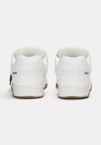 Vita sneakers med en slät läderövre, vadderad krage och sula av gummigummi. Bakåtsidan visar sömnad och logodetaljer nära hälen.