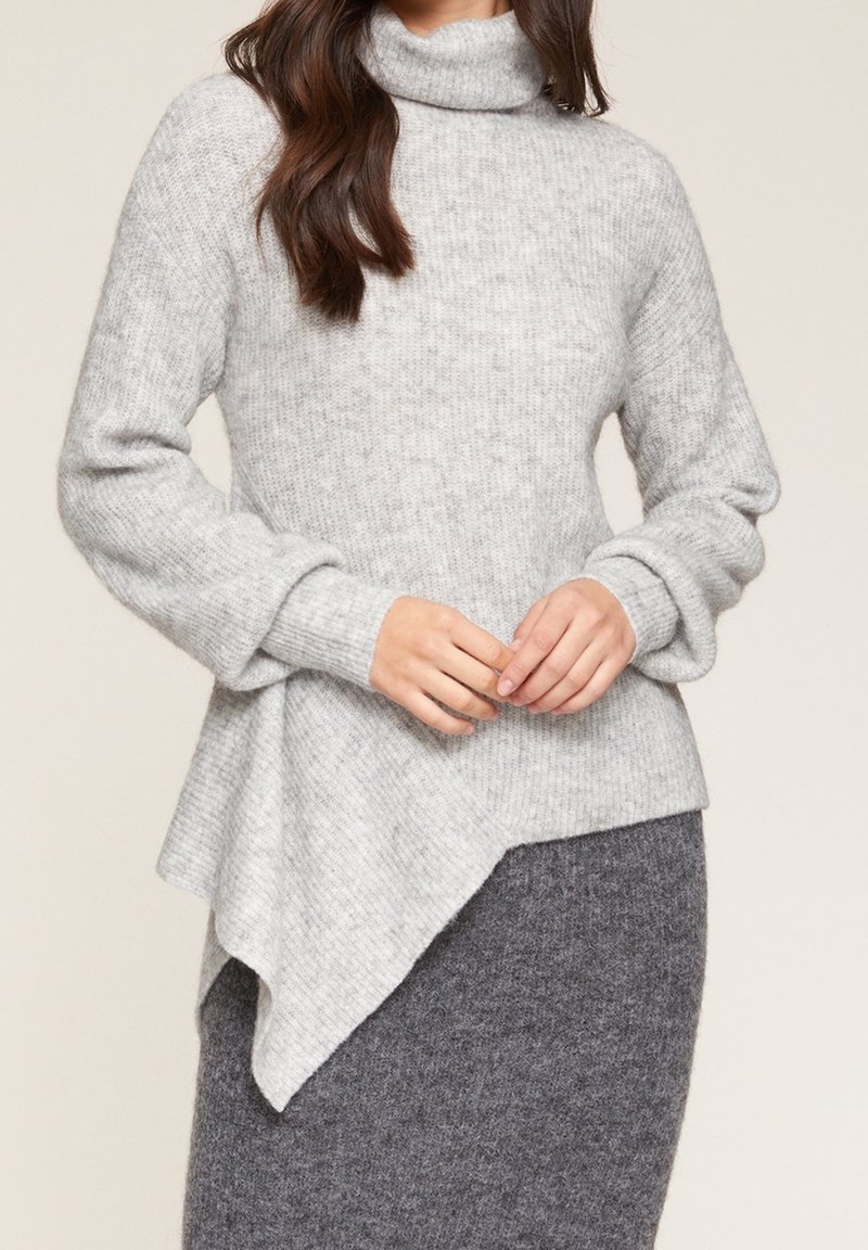 Grauer wollener Rollkragenpullover mit langen Ärmeln, der über ein strukturiertes Strickmuster und ein asymmetrisches Saumdesign verfügt, kombiniert mit einem dunkelgrauen Rock.
