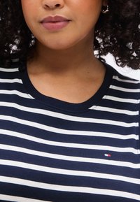 Μπλούζα με ριγέ σχεδίαση σε ναυτικό μπλε και λευκό, κατασκευασμένη από βαμβάκι· διαθέτει στρογγυλή λαιμόκοψη και μικρό λογότυπο με κόκκινες, λευκές και μπλε αποχρώσεις στο στήθος.