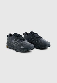 Un paio di scarpe da trail running nere con suole testurizzate, tomaia in rete, design con lacci e dettagli riflettenti del logo su uno sfondo grigio chiaro.