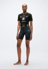 Ensemble sportif UFC noir comprenant un haut à manches courtes avec un motif texturé et un short de compression assorti avec un design géométrique.