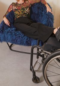 Fauteuil en fausse fourrure bleu profond, doté d'une forme arrondie avec une surface texturée. Fauteuil roulant noir avec cadre en métal et roues en caoutchouc à proximité.