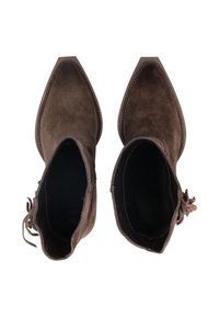 Botas de tobillo de ante marrón con punta afilada, diseño minimalista y un detalle de encaje en un lado. El interior es oscuro y tiene una textura suave.