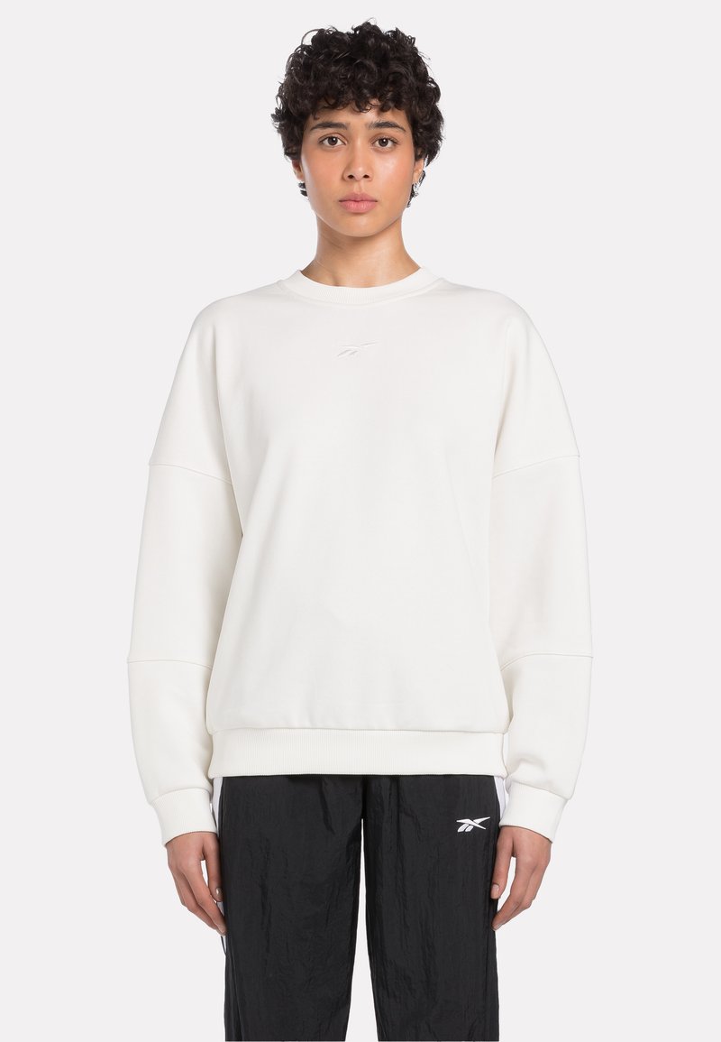 Weißes Sweatshirt mit Rundhalsausschnitt, überschnittenen Schultern, gerippten Bündchen und kleinem Logo auf der Brust, kombiniert mit schwarzen Hosen.