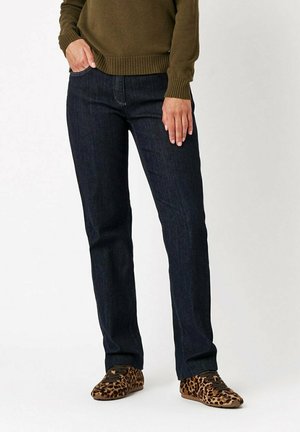 Jeans blu scuro con taglio dritto, realizzati in denim. Abbinati a un maglione verde e sneakers con stampa leopardata. Design semplice, senza hardware visibile.