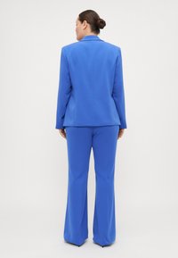 Blazer entallado azul y traje de pantalón a juego, con una textura de tela suave, diseño ajustado y piernas de pantalón ligeramente acampanadas.