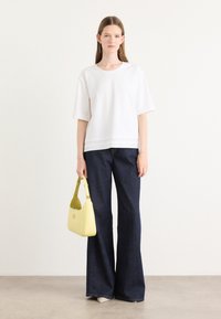 Hvit kortermet topp, mørkeblå vidde jeans og en gul skulderveske med rund aksent. Enkelt design, teksturert stoff.