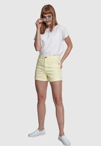 Pantaloni scurți din denim galben cu manșete răsucite, talie înaltă și închidere cu un buton; asortați cu un tricou alb simplu și pantofi slip-on albi.
